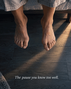 Bare feet hesitating at the edge of a bed on a hardwood floor — the familiar pause before the first painful step