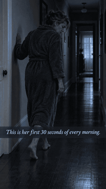 Woman in a dark hallway touching the wall for support — the first 30 seconds of every morning.