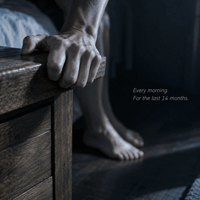 Close-up of a hand gripping a nightstand for support — caption reads: Every morning. For the last 14 months.